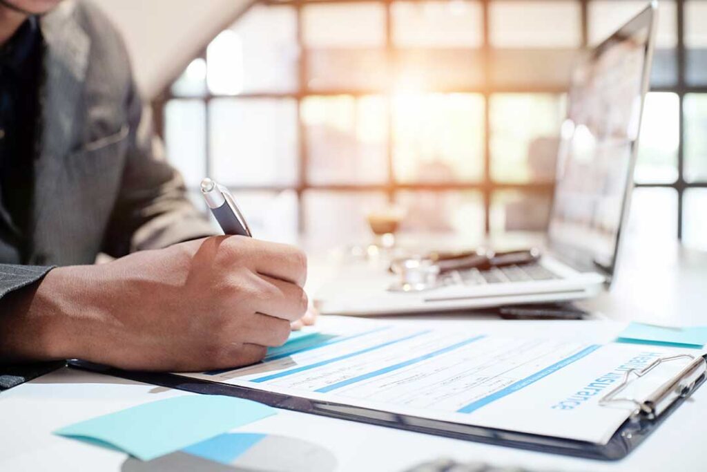 Former spouses review insurance papers, vehicle documents, and a home policy at a kitchen table.